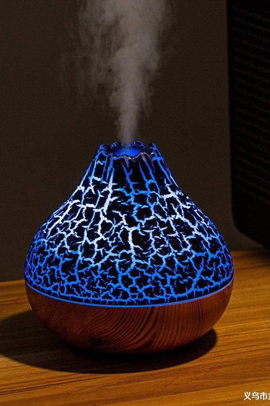 Volcano-shaped humidifier with glowing blue crackle light and cool mist on wooden surface