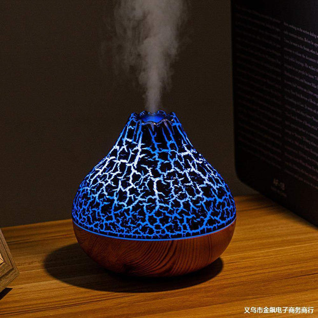 Volcano-shaped humidifier with glowing blue crackle light and cool mist on wooden surface