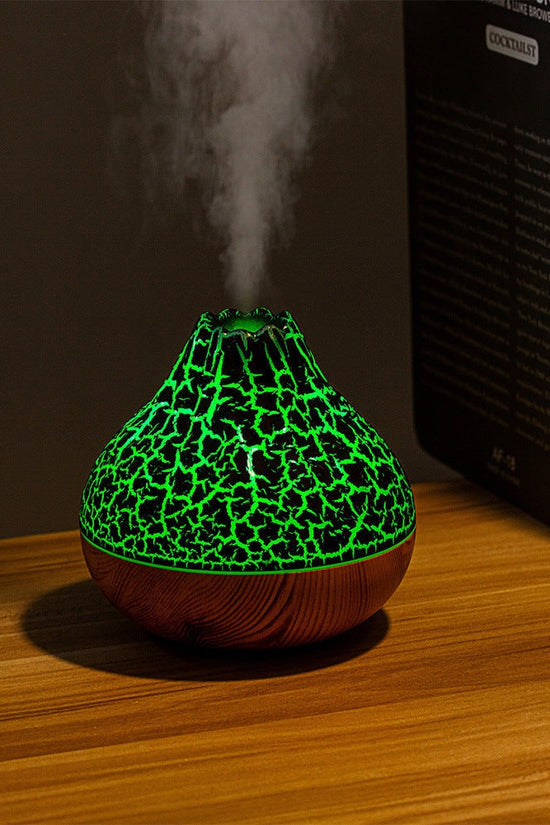 Volcano-shaped humidifier with green glowing cracked pattern and wood grain base emitting cool mist on wooden table