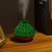 Volcano-shaped humidifier with green glowing cracked pattern and wood grain base emitting cool mist on wooden table