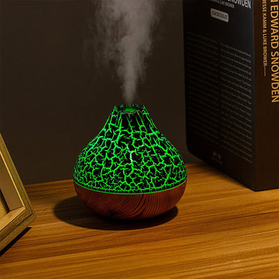 Volcano-shaped humidifier with green glowing cracked pattern and wood grain base emitting cool mist on wooden table
